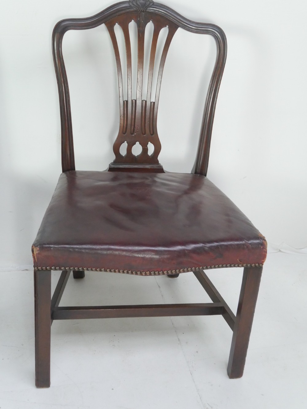A set of eight mahogany Chippendale style dining chairs featuring pierced splat backs, square legs with stretchers, and burgundy leather seats trimmed with brass studs. View V