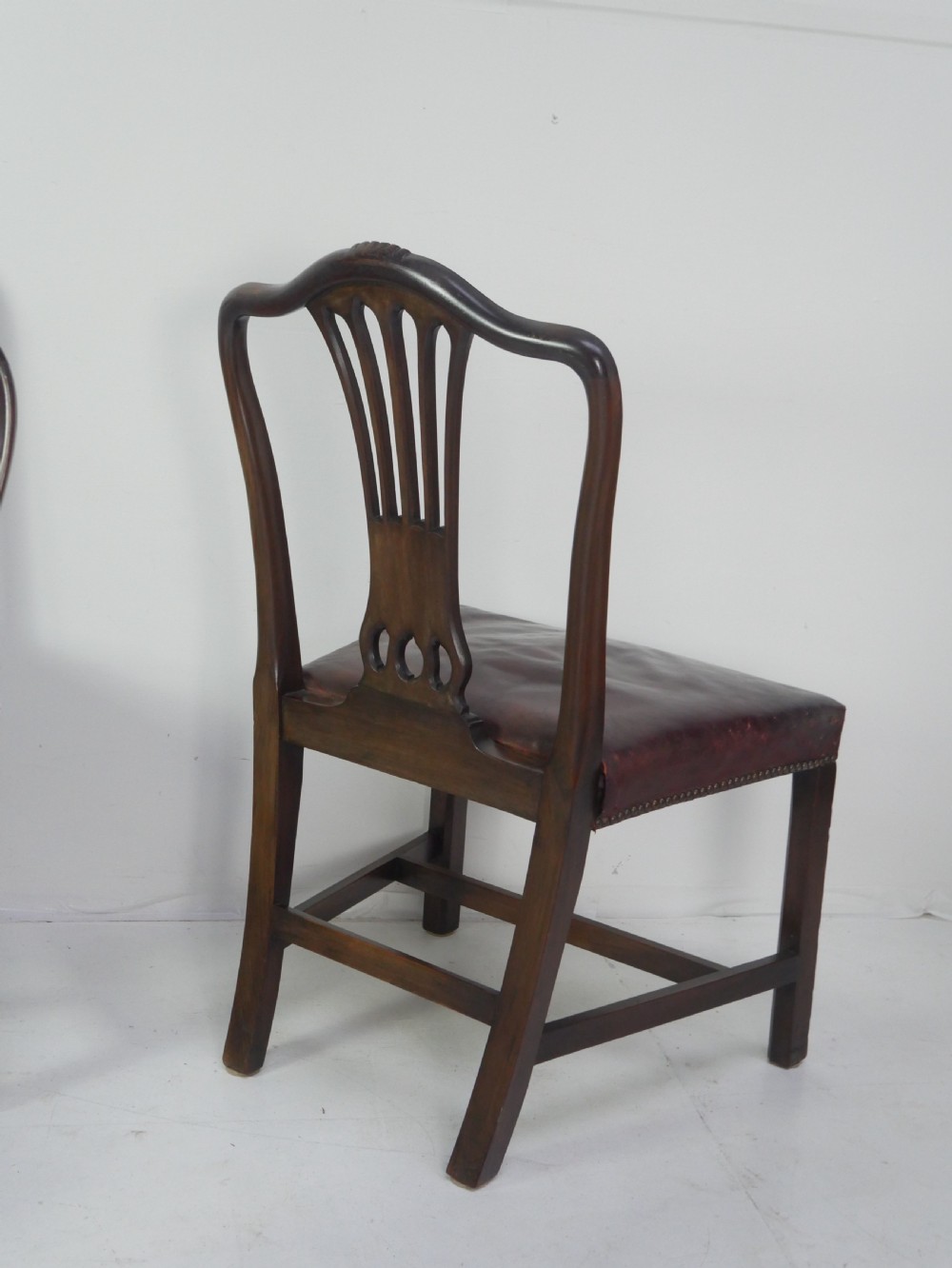 A set of eight mahogany Chippendale style dining chairs featuring pierced splat backs, square legs with stretchers, and burgundy leather seats trimmed with brass studs. View IX