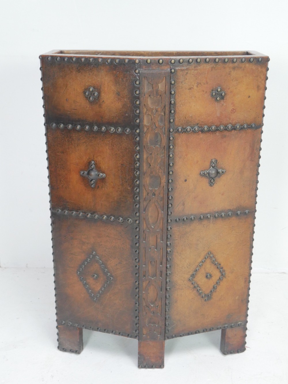 A tall, angular brown leather umbrella stand crafted with studded metal borders and decorative embossed detailing. View V