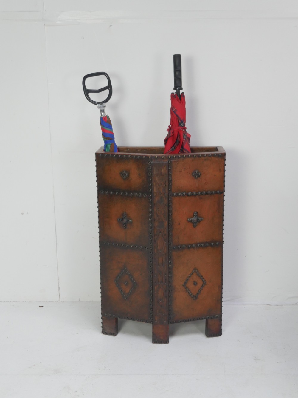 A tall, angular brown leather umbrella stand crafted with studded metal borders and decorative embossed detailing.