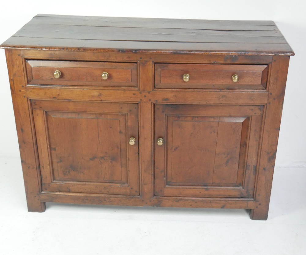 A Georgian oak dresser base featuring two top drawers above two fielded panel cupboard doors fitted with small brass knobs. View V