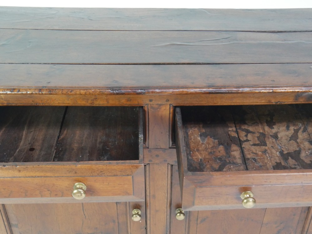 A Georgian oak dresser base featuring two top drawers above two fielded panel cupboard doors fitted with small brass knobs. View VI
