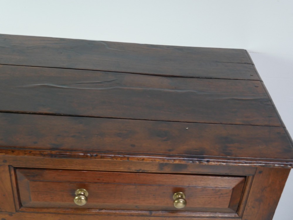 A Georgian oak dresser base featuring two top drawers above two fielded panel cupboard doors fitted with small brass knobs. View X
