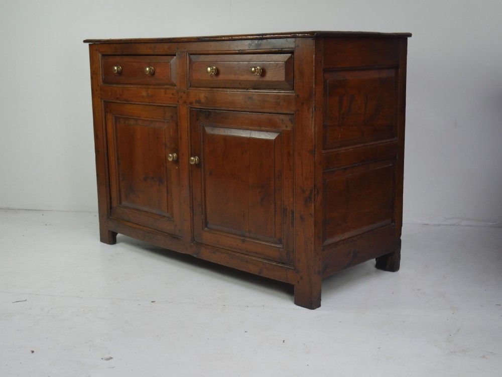 A Georgian oak dresser base featuring two top drawers above two fielded panel cupboard doors fitted with small brass knobs. View XII