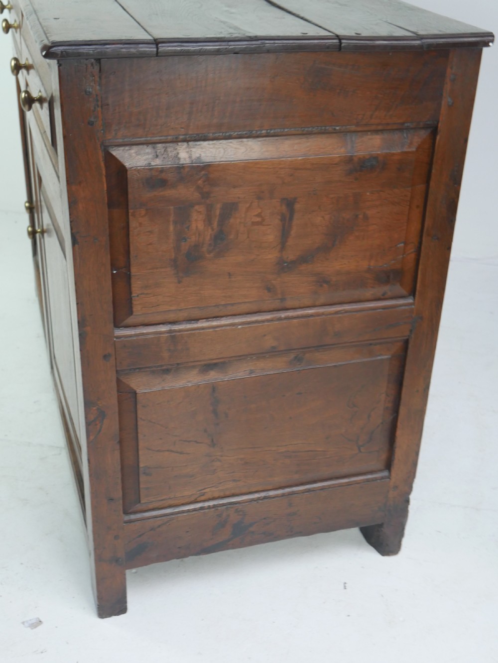 A Georgian oak dresser base featuring two top drawers above two fielded panel cupboard doors fitted with small brass knobs. View XIII