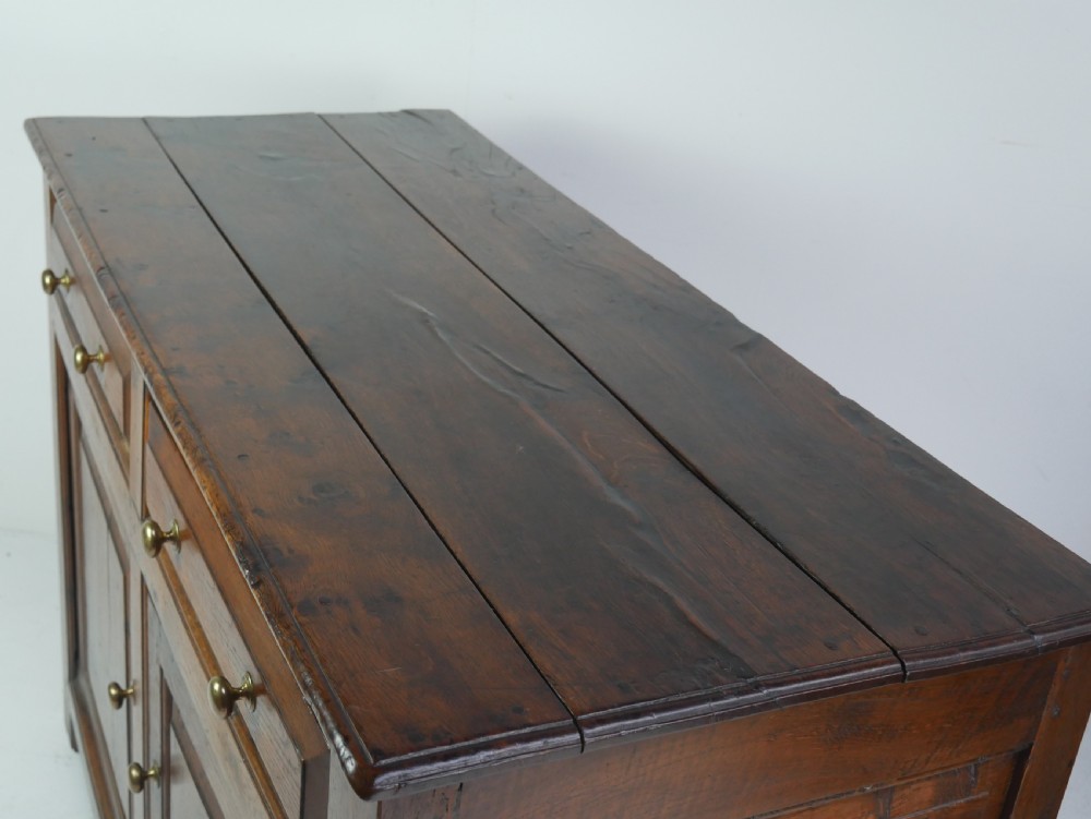 A Georgian oak dresser base featuring two top drawers above two fielded panel cupboard doors fitted with small brass knobs. View XV