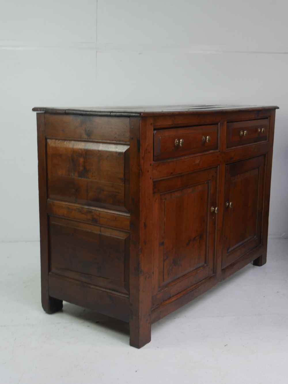 A Georgian oak dresser base featuring two top drawers above two fielded panel cupboard doors fitted with small brass knobs. View XVI