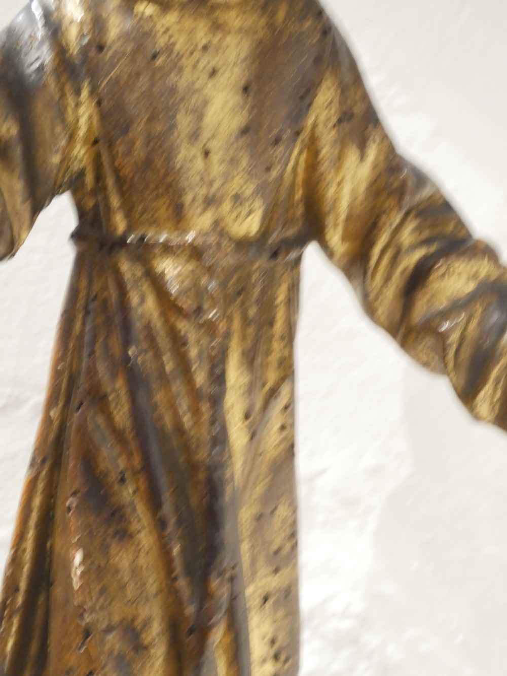 A carved giltwood figure depicting Saint Francis in draped monastic robes standing on a dark wooden plinth. View V
