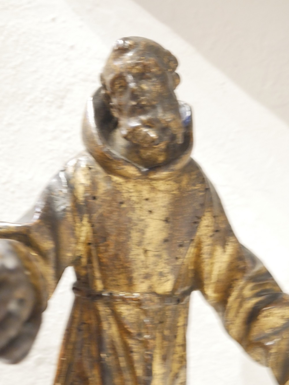 A carved giltwood figure depicting Saint Francis in draped monastic robes standing on a dark wooden plinth. View VI
