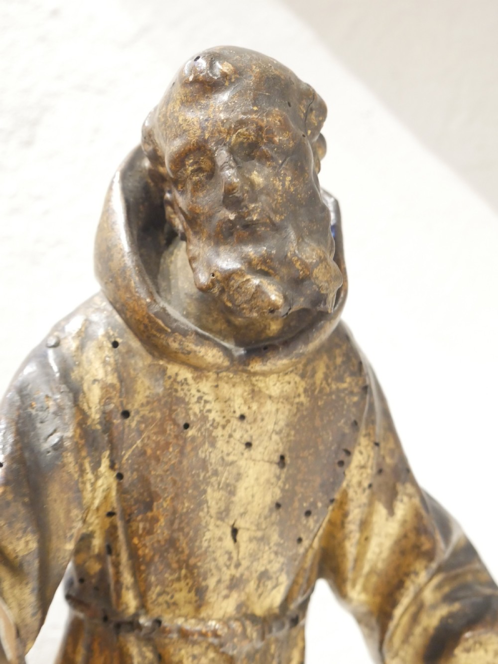 A carved giltwood figure depicting Saint Francis in draped monastic robes standing on a dark wooden plinth. View VII