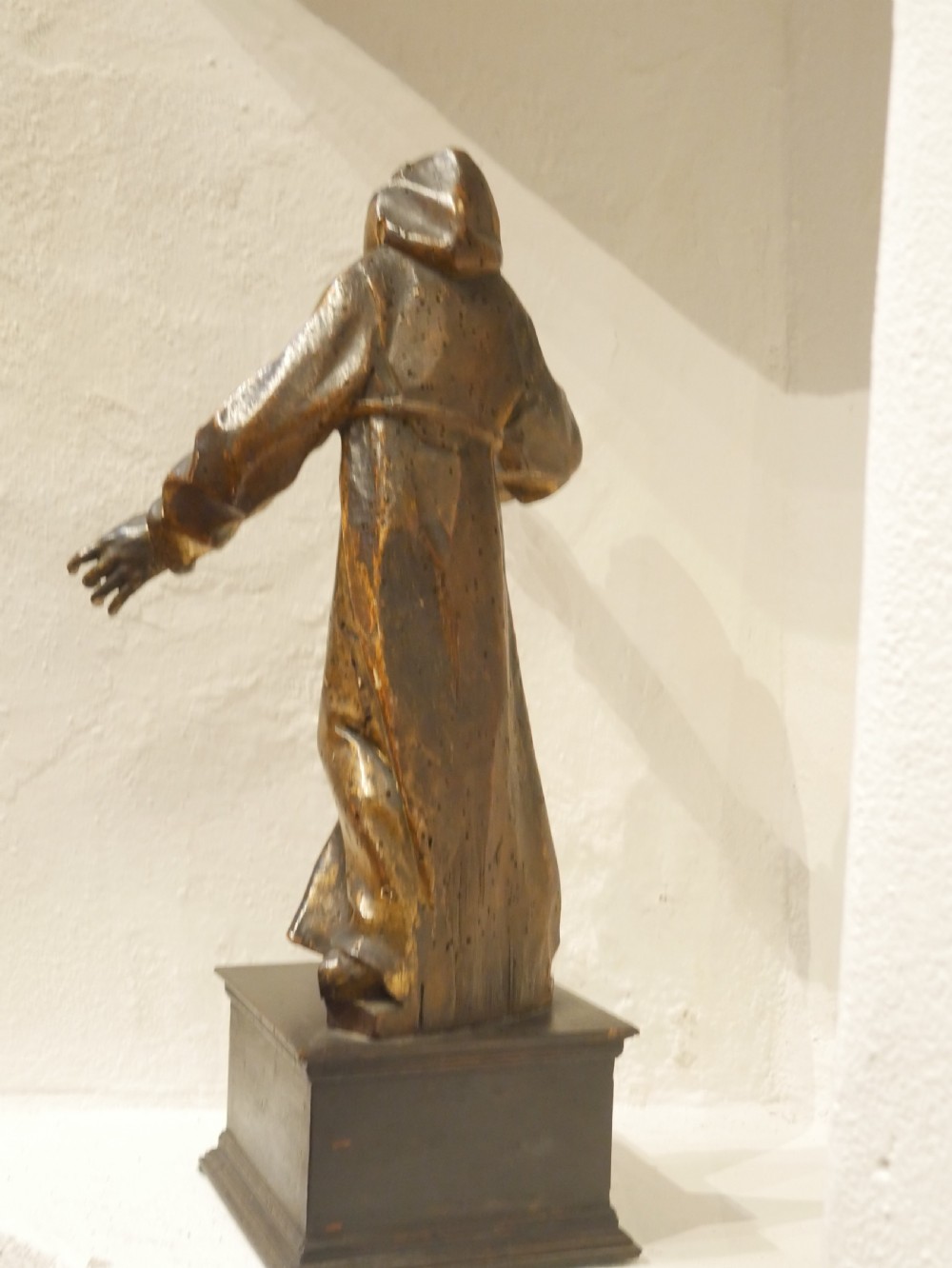 A carved giltwood figure depicting Saint Francis in draped monastic robes standing on a dark wooden plinth. View XI