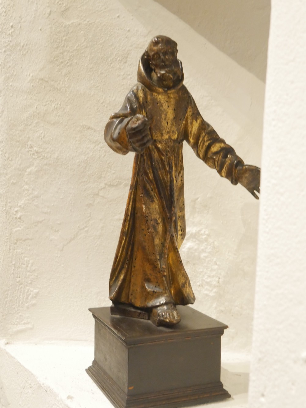 A carved giltwood figure depicting Saint Francis in draped monastic robes standing on a dark wooden plinth. View XII