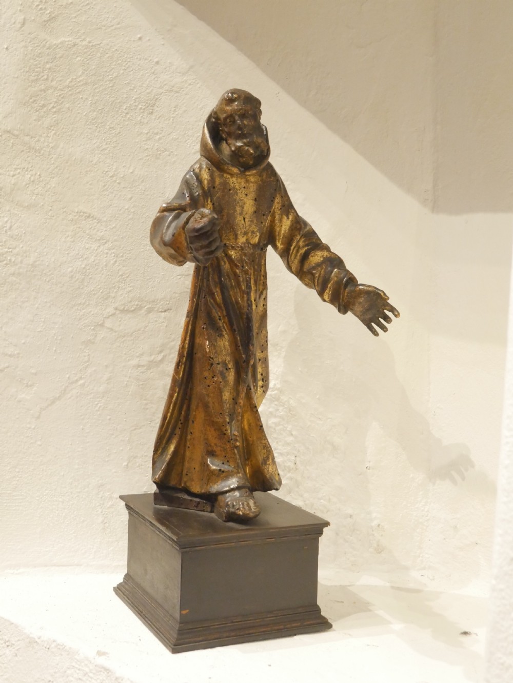 A carved giltwood figure depicting Saint Francis in draped monastic robes standing on a dark wooden plinth. View XVI