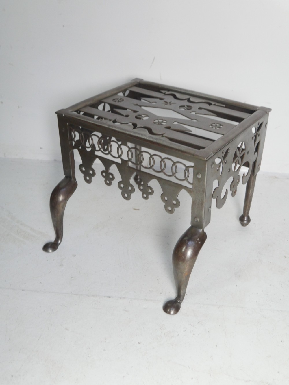 An antique pierced steel hearth footman featuring cabriole front legs, pad feet, and a fretted top.