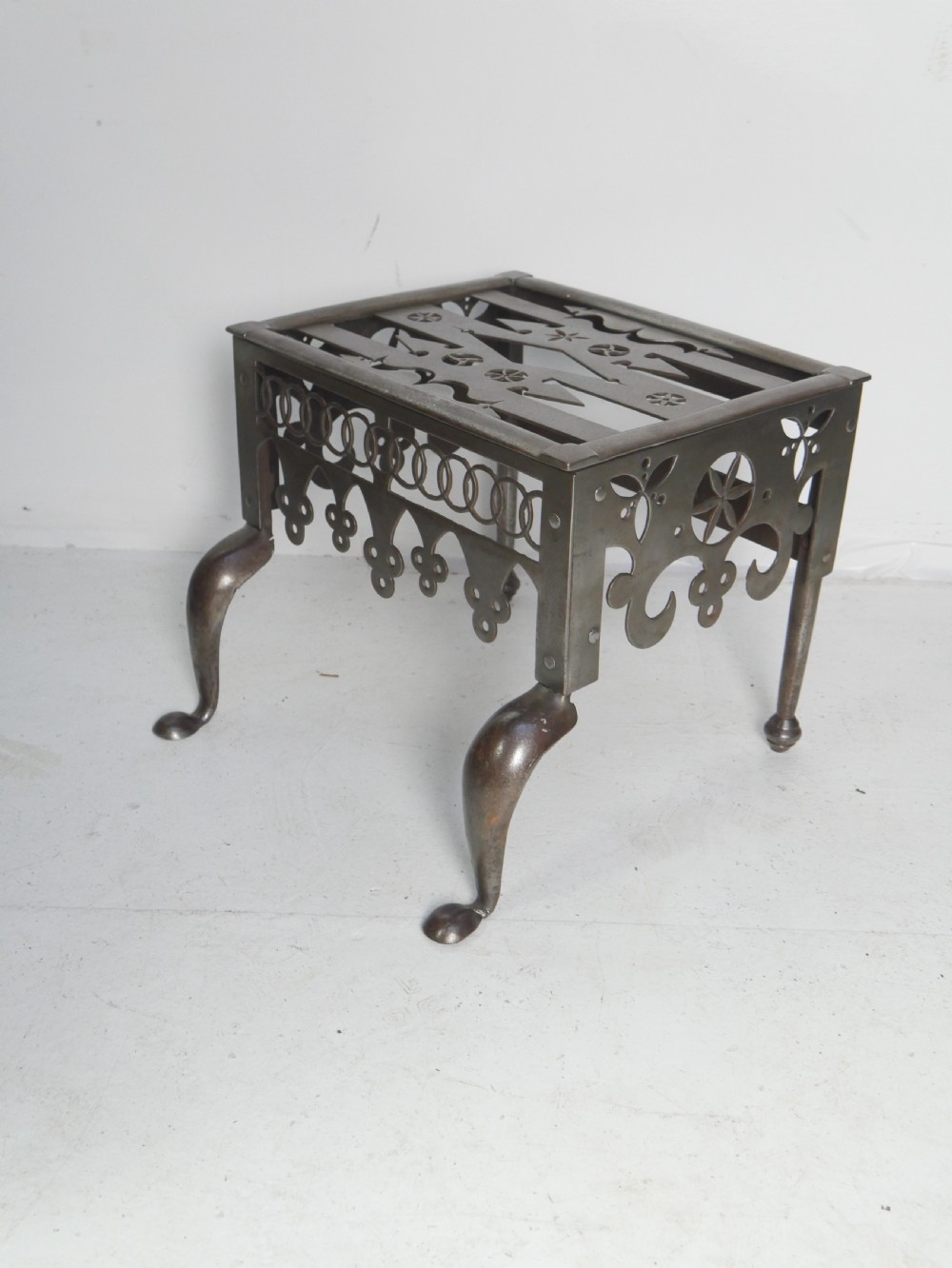 An antique pierced steel hearth footman featuring cabriole front legs, pad feet, and a fretted top. View V