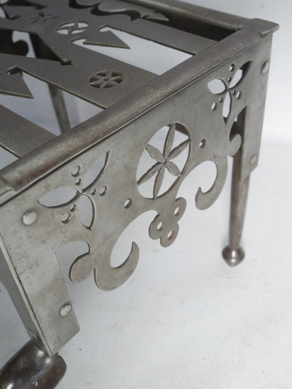 An antique pierced steel hearth footman featuring cabriole front legs, pad feet, and a fretted top. View IX