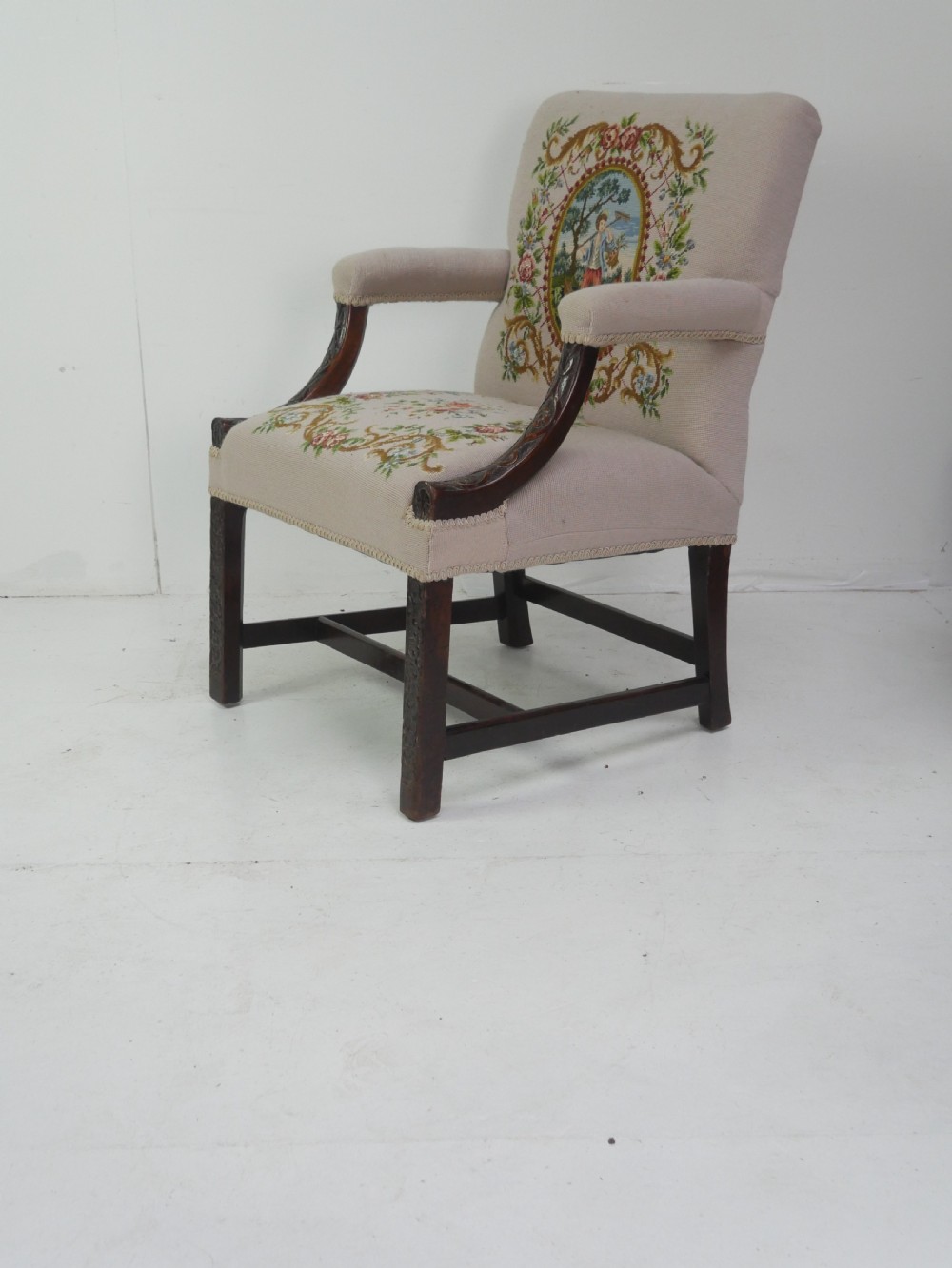 A Georgian Gainsborough armchair with dark carved mahogany legs, upholstered in beige needlepoint tapestry featuring a central pastoral scene and floral borders. View XI