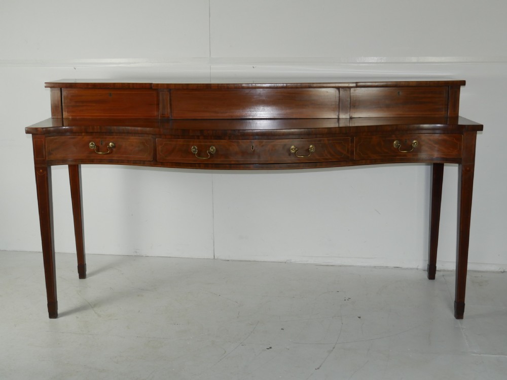 A Scottish Georgian mahogany sideboard featuring a raised stage top superstructure, stringing inlay, three drawer fronts with brass drop handles, and square tapered legs.
