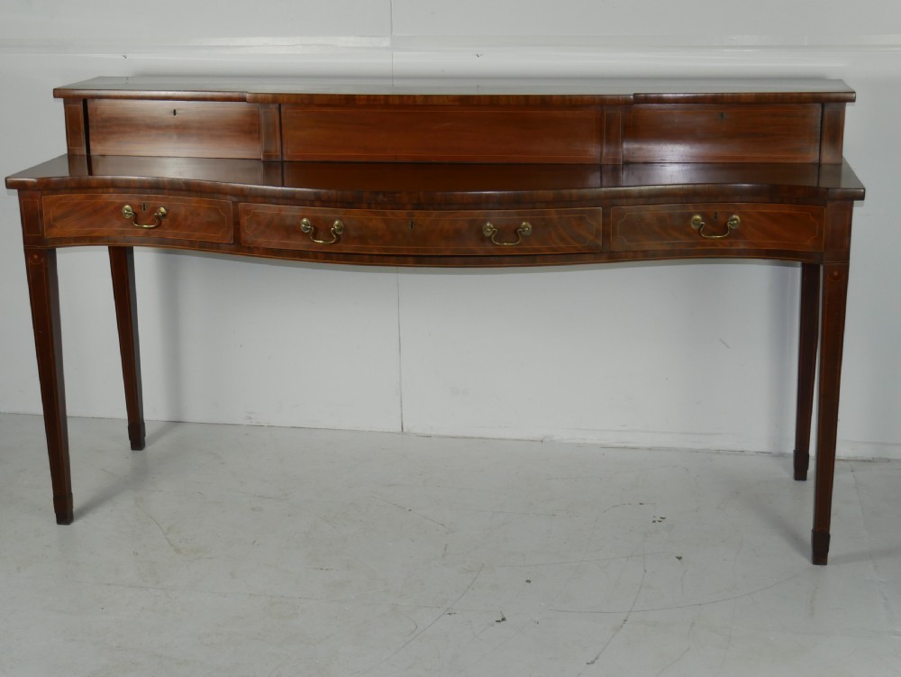 A Scottish Georgian mahogany sideboard featuring a raised stage top superstructure, stringing inlay, three drawer fronts with brass drop handles, and square tapered legs. View X