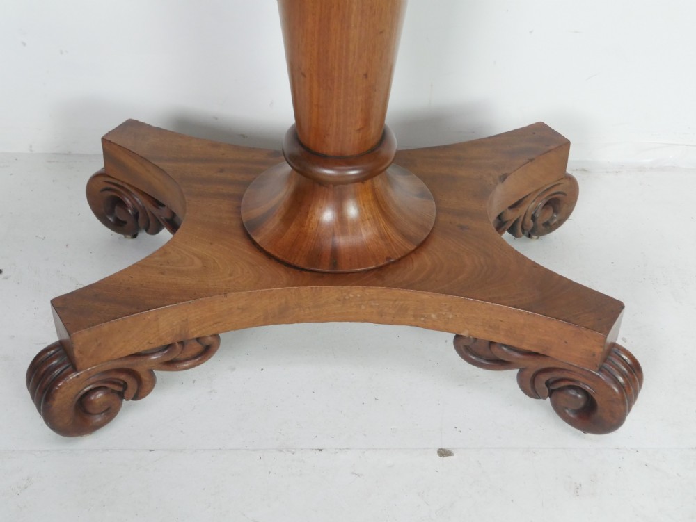 A 19th-century mahogany turn-over table featuring a fold-over top, carved corner scroll accents, a tapered pedestal, and a quadform platform base with scroll feet. View II
