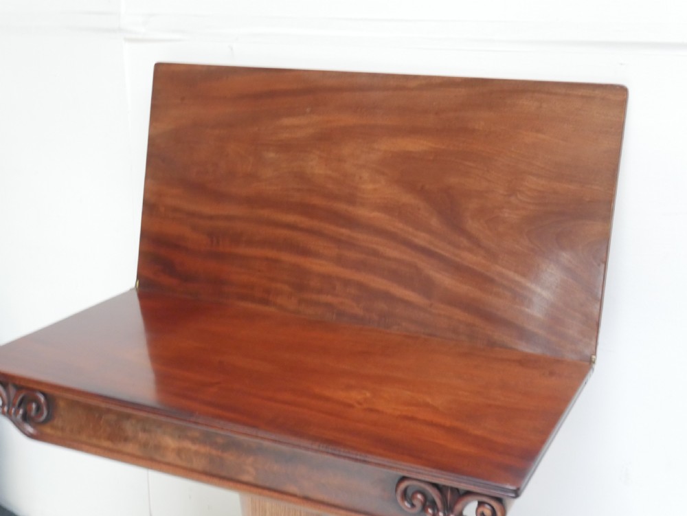 A 19th-century mahogany turn-over table featuring a fold-over top, carved corner scroll accents, a tapered pedestal, and a quadform platform base with scroll feet. View III