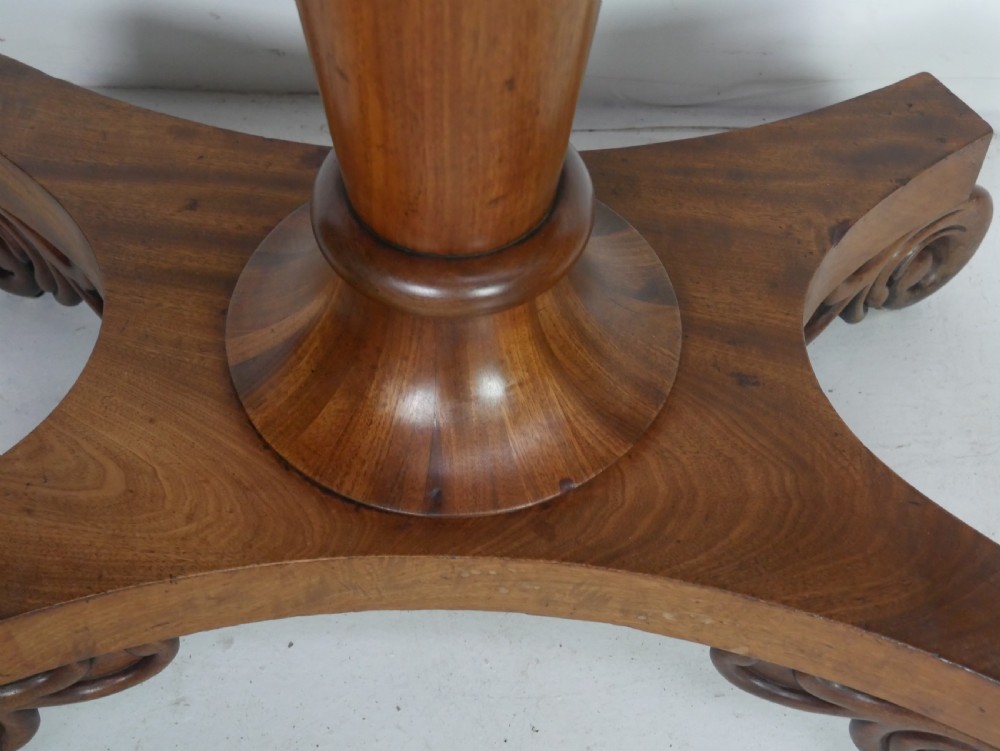 A 19th-century mahogany turn-over table featuring a fold-over top, carved corner scroll accents, a tapered pedestal, and a quadform platform base with scroll feet. View VI