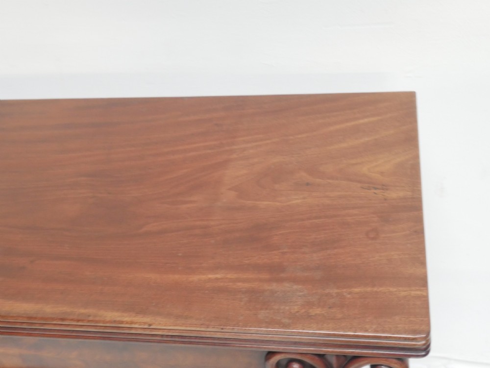A 19th-century mahogany turn-over table featuring a fold-over top, carved corner scroll accents, a tapered pedestal, and a quadform platform base with scroll feet. View VIII
