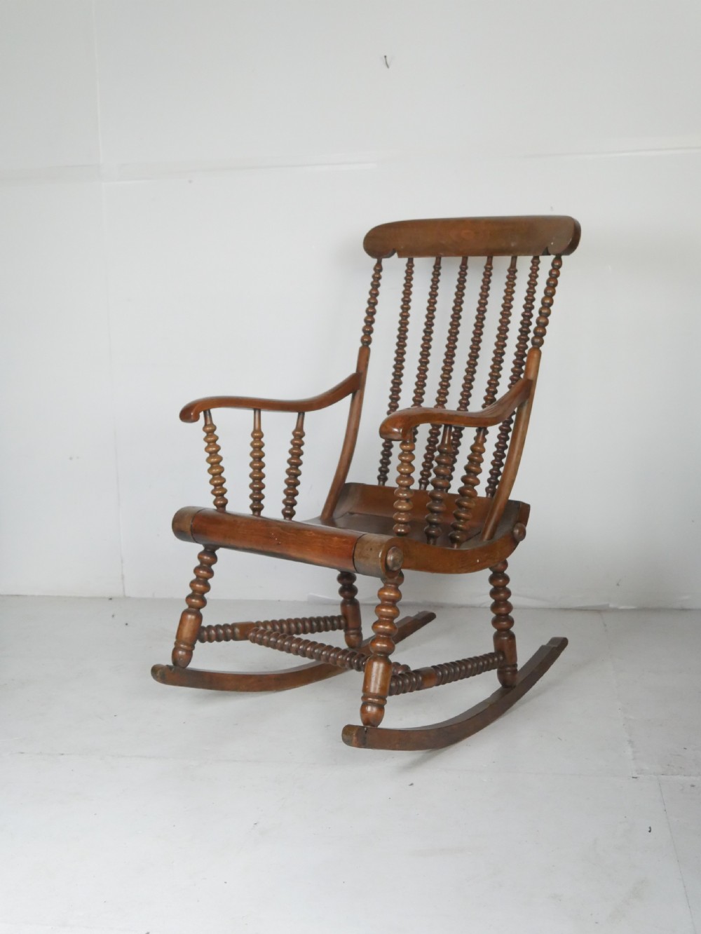 An antique warm brown wooden rocking chair featuring intricate bobbin-turned spindles along the backrest, armrests, legs, and stretchers.