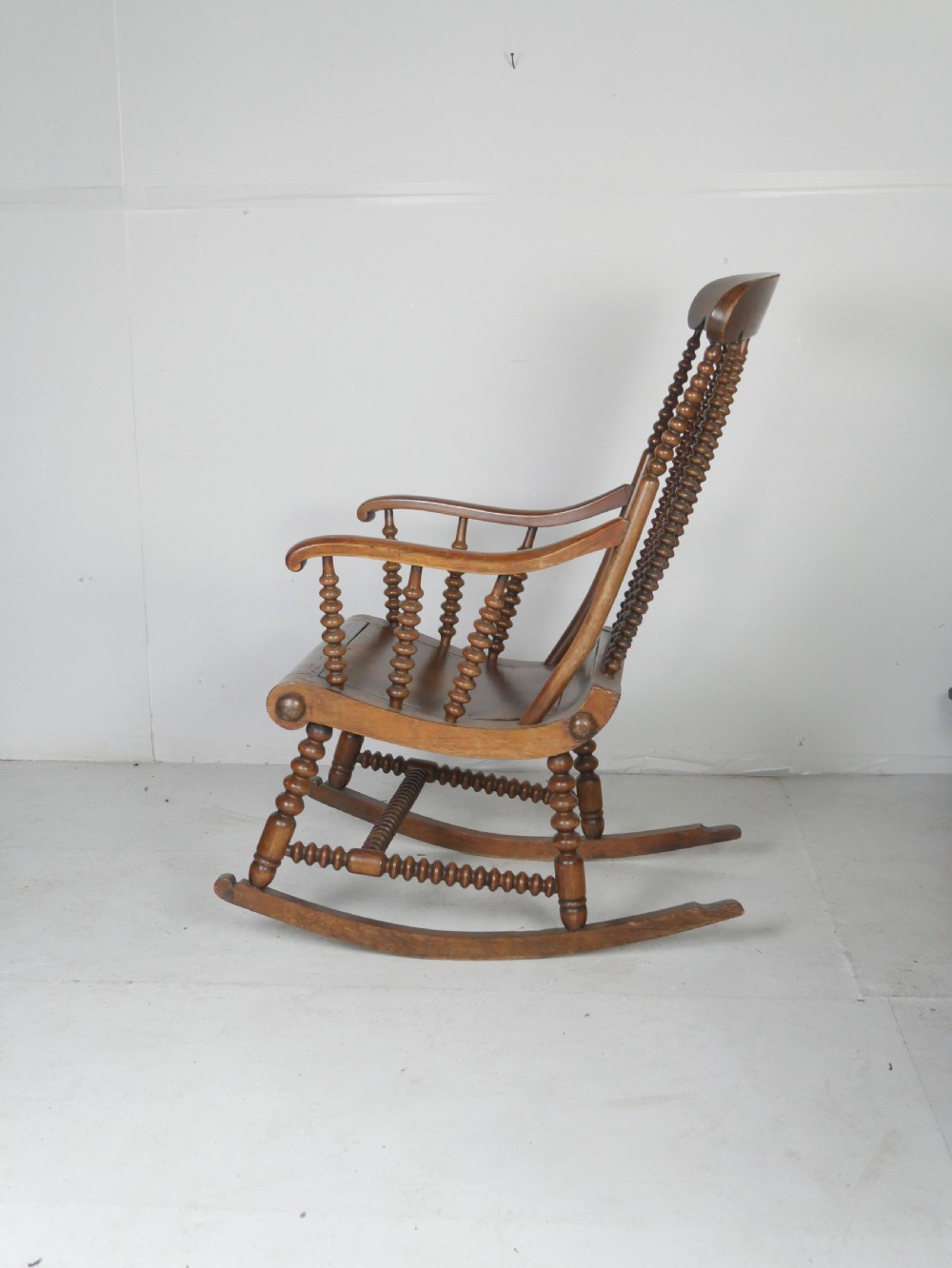 An antique warm brown wooden rocking chair featuring intricate bobbin-turned spindles along the backrest, armrests, legs, and stretchers. View II