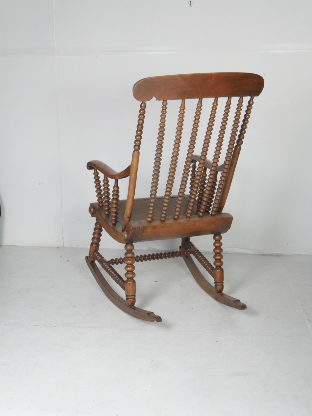 An antique warm brown wooden rocking chair featuring intricate bobbin-turned spindles along the backrest, armrests, legs, and stretchers. View III