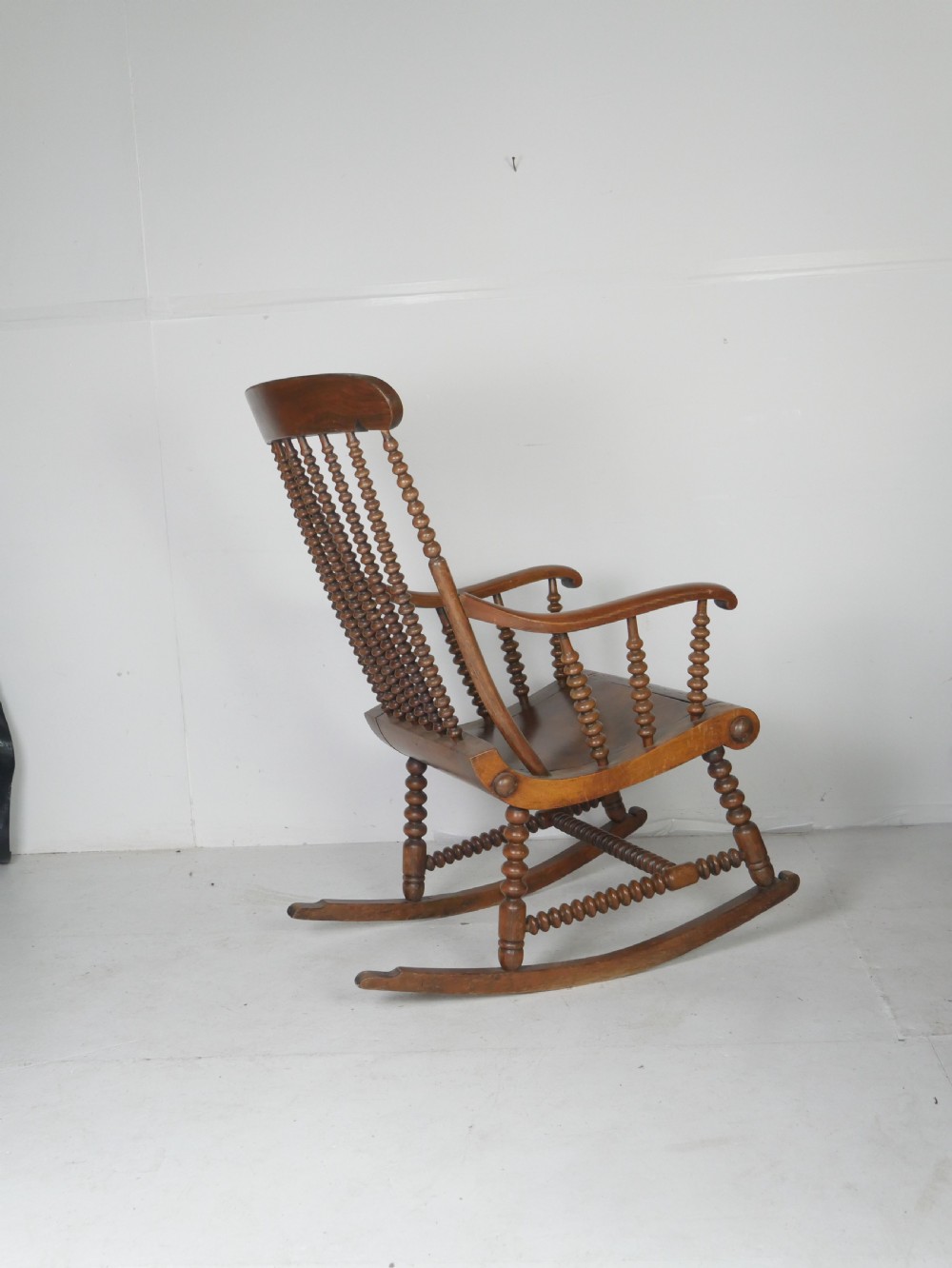 An antique warm brown wooden rocking chair featuring intricate bobbin-turned spindles along the backrest, armrests, legs, and stretchers. View V