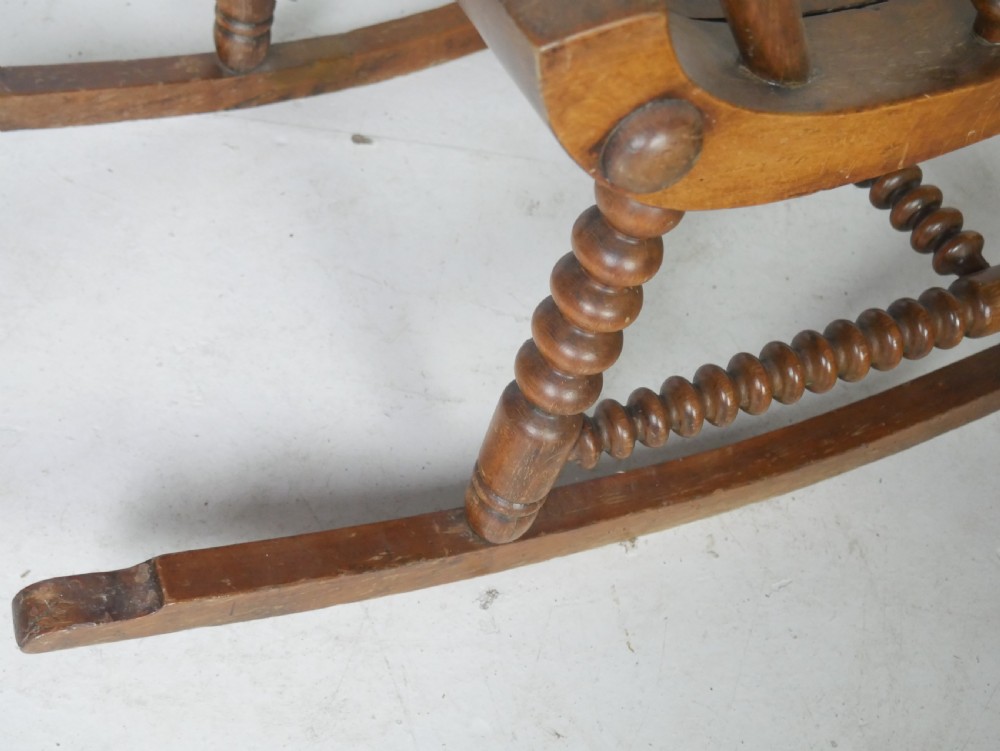 An antique warm brown wooden rocking chair featuring intricate bobbin-turned spindles along the backrest, armrests, legs, and stretchers. View VI