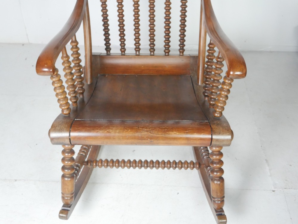 An antique warm brown wooden rocking chair featuring intricate bobbin-turned spindles along the backrest, armrests, legs, and stretchers. View IX