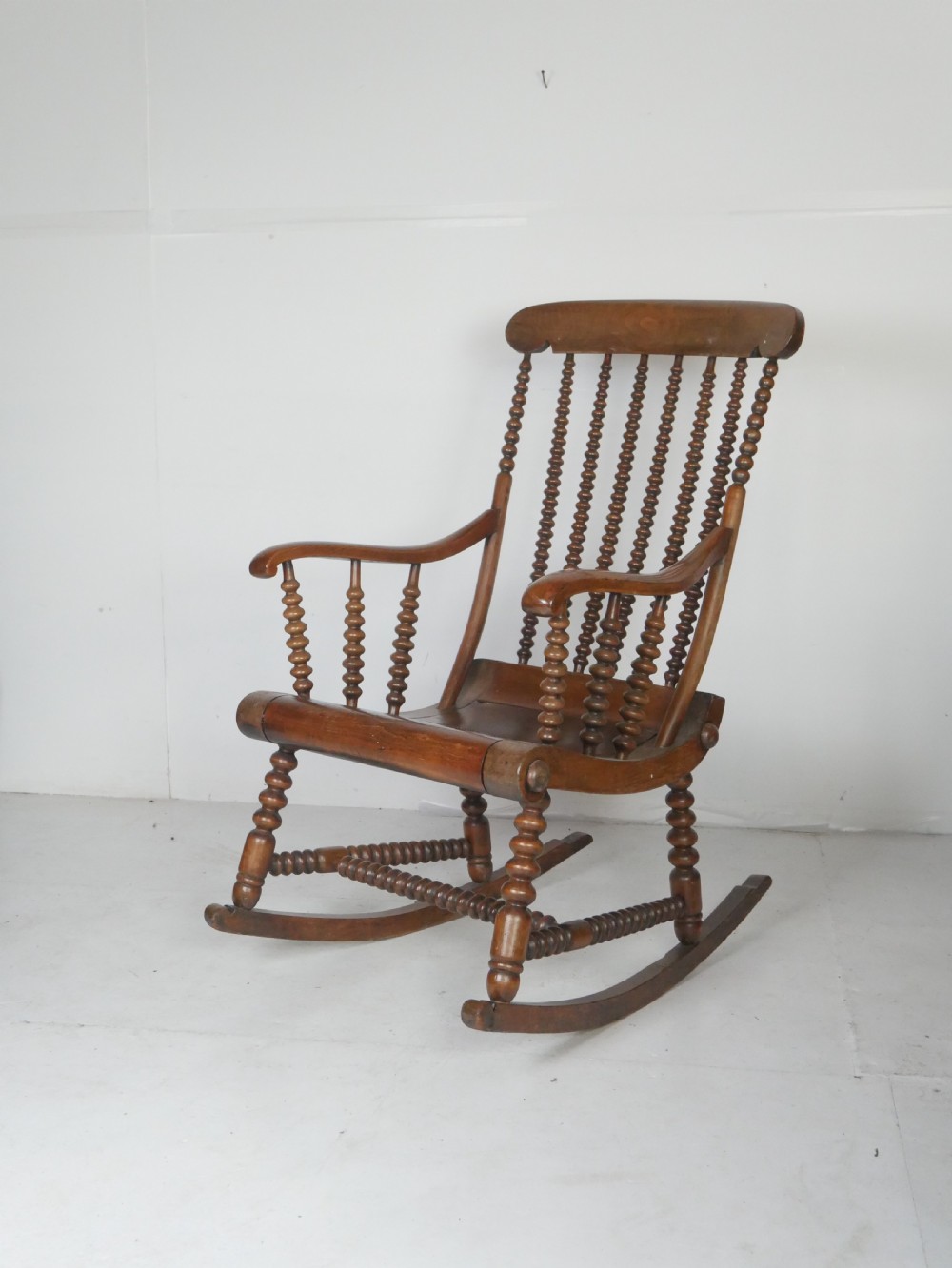 An antique warm brown wooden rocking chair featuring intricate bobbin-turned spindles along the backrest, armrests, legs, and stretchers. View X