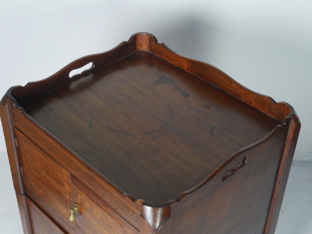 A Georgian mahogany bedside cabinet featuring a tray top gallery, two cupboard doors with string inlay, and two drawers with brass swan-neck handles. View IV