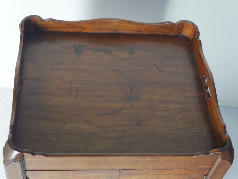 A Georgian mahogany bedside cabinet featuring a tray top gallery, two cupboard doors with string inlay, and two drawers with brass swan-neck handles. View V