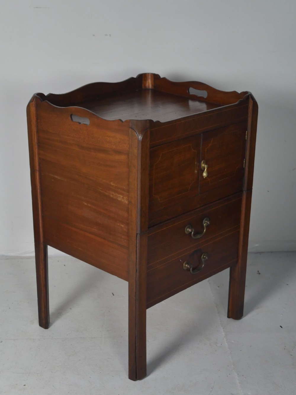 A Georgian mahogany bedside cabinet featuring a tray top gallery, two cupboard doors with string inlay, and two drawers with brass swan-neck handles. View VI