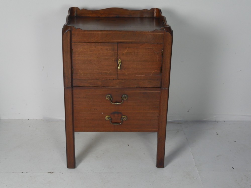 A Georgian mahogany bedside cabinet featuring a tray top gallery, two cupboard doors with string inlay, and two drawers with brass swan-neck handles. View X