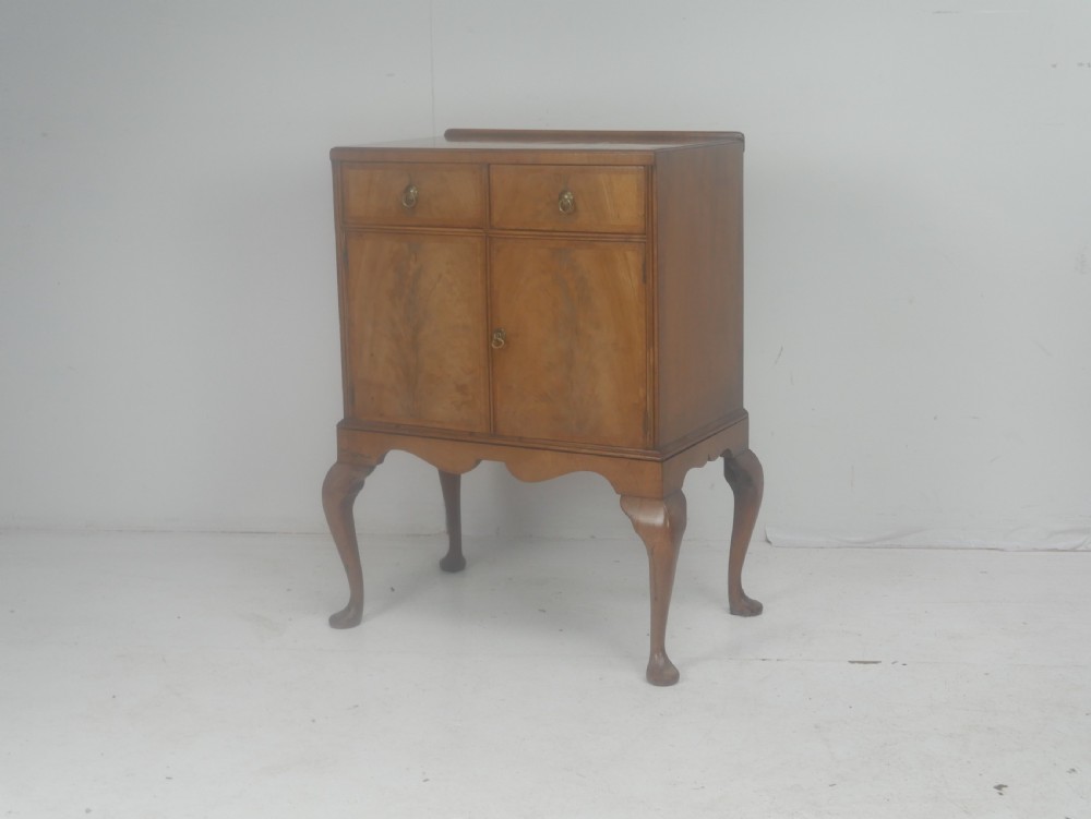 A Queen Anne revival walnut bedside cabinet featuring two top drawers, a two-door cupboard, and tall cabriole legs.