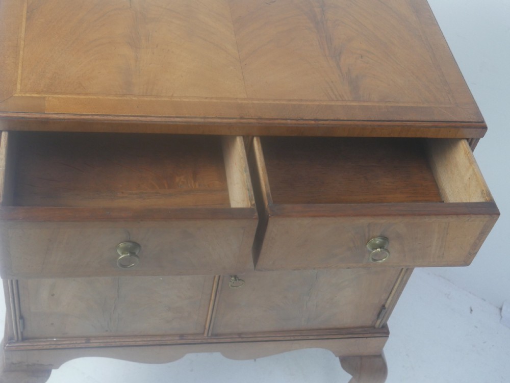 A Queen Anne revival walnut bedside cabinet featuring two top drawers, a two-door cupboard, and tall cabriole legs. View XV
