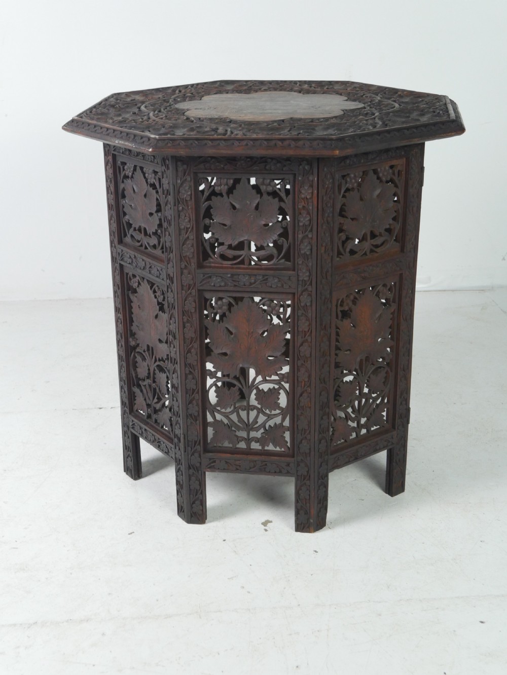 An octagonal dark wood side table featuring hand-carved foliage fretwork on all side panels and a relief carved top.