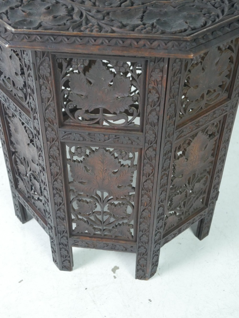 An octagonal dark wood side table featuring hand-carved foliage fretwork on all side panels and a relief carved top. View II