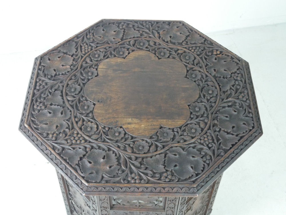 An octagonal dark wood side table featuring hand-carved foliage fretwork on all side panels and a relief carved top. View VII