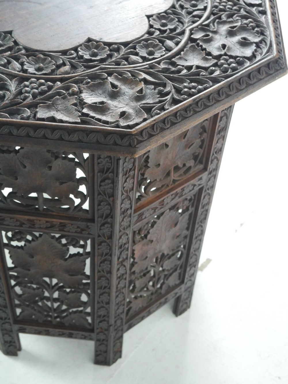 An octagonal dark wood side table featuring hand-carved foliage fretwork on all side panels and a relief carved top. View VIII