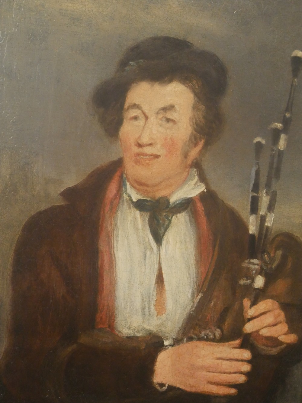 An oil portrait on canvas depicting a male Northumbrian piper holding smallpipes, housed in an ornate carved gilt frame. View V