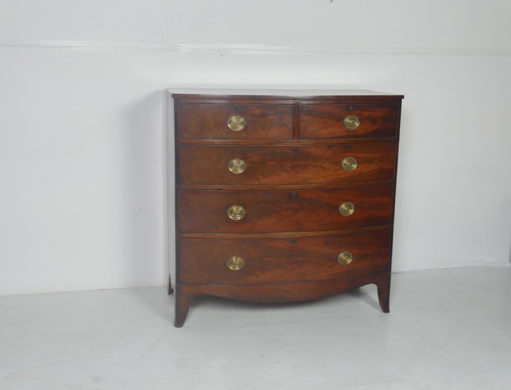 An early nineteenth-century mahogany bow-front chest of drawers featuring two short drawers over three long drawers with oval brass handles and splayed feet.