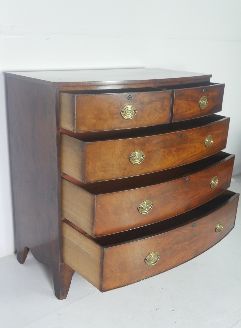 An early nineteenth-century mahogany bow-front chest of drawers featuring two short drawers over three long drawers with oval brass handles and splayed feet. View II