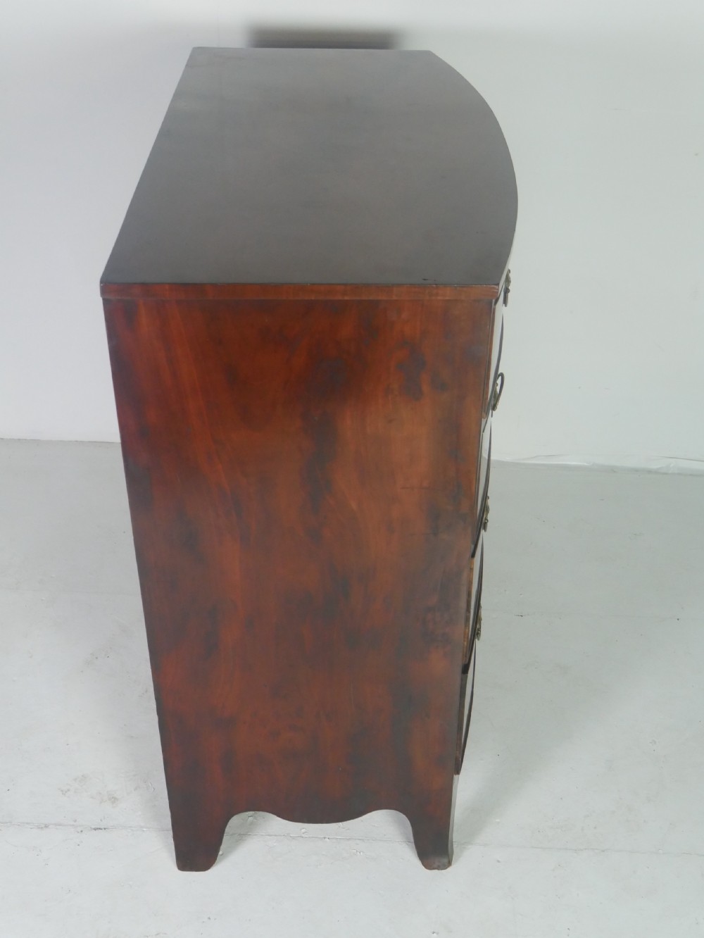 An early nineteenth-century mahogany bow-front chest of drawers featuring two short drawers over three long drawers with oval brass handles and splayed feet. View III
