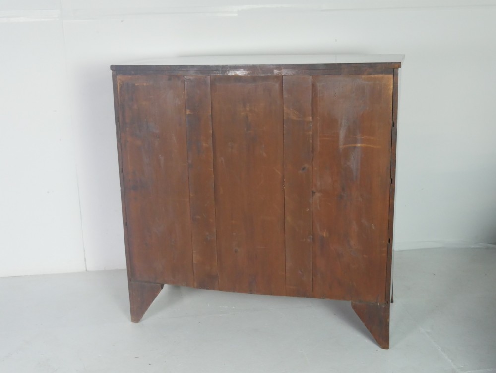 An early nineteenth-century mahogany bow-front chest of drawers featuring two short drawers over three long drawers with oval brass handles and splayed feet. View IV