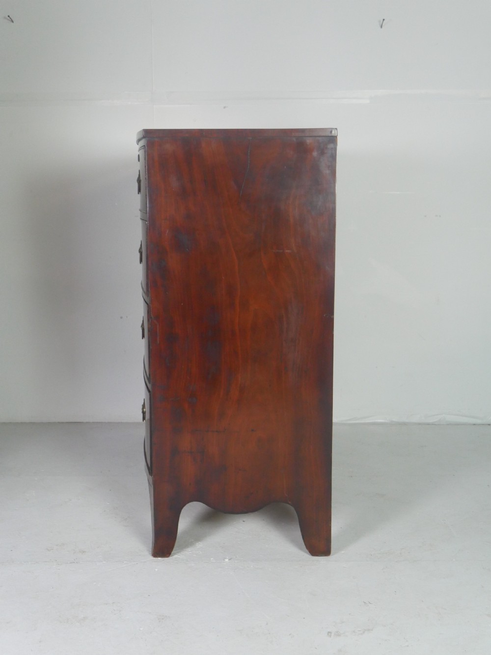 An early nineteenth-century mahogany bow-front chest of drawers featuring two short drawers over three long drawers with oval brass handles and splayed feet. View V